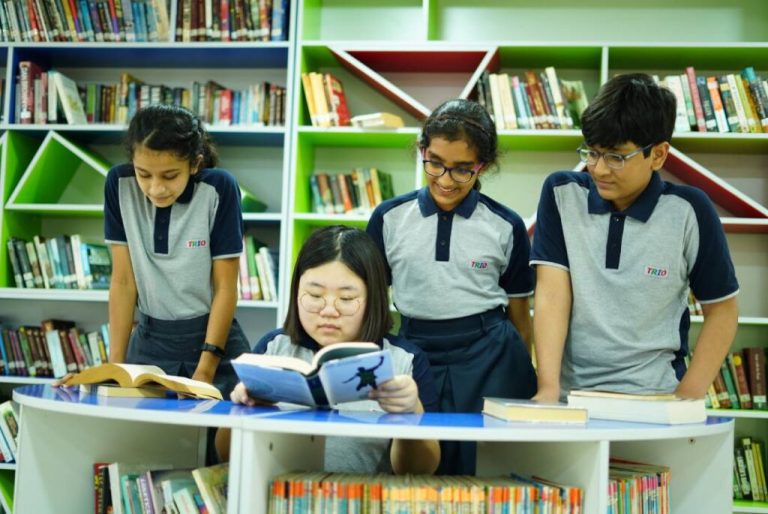 students learning from other students from a book in the library to show how are internatiopnal schools different